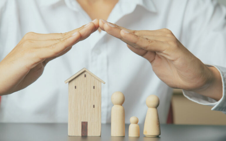 Hands over wooden model home and family