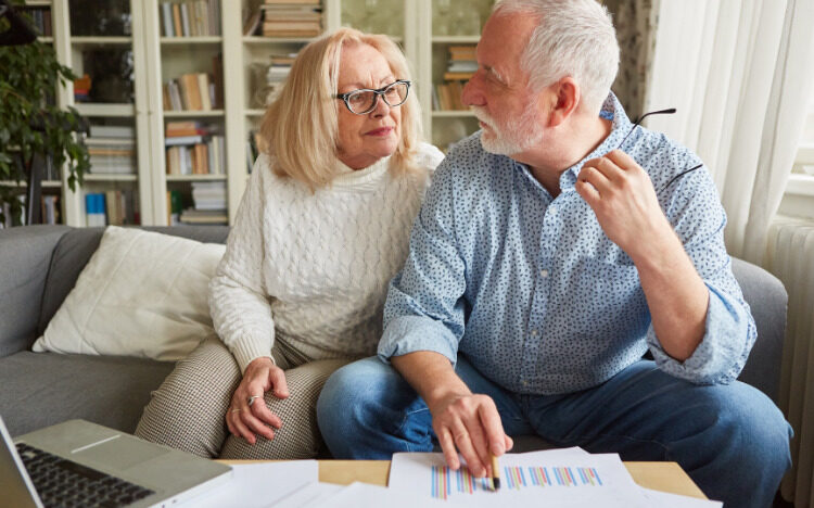 Older couple on couch with paperwork discussing finances