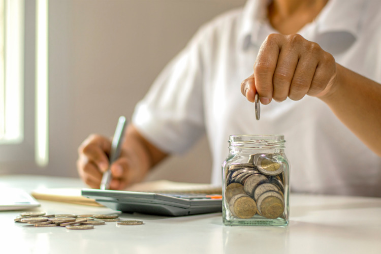 Man at desk putting coins into jar with calculator and pen